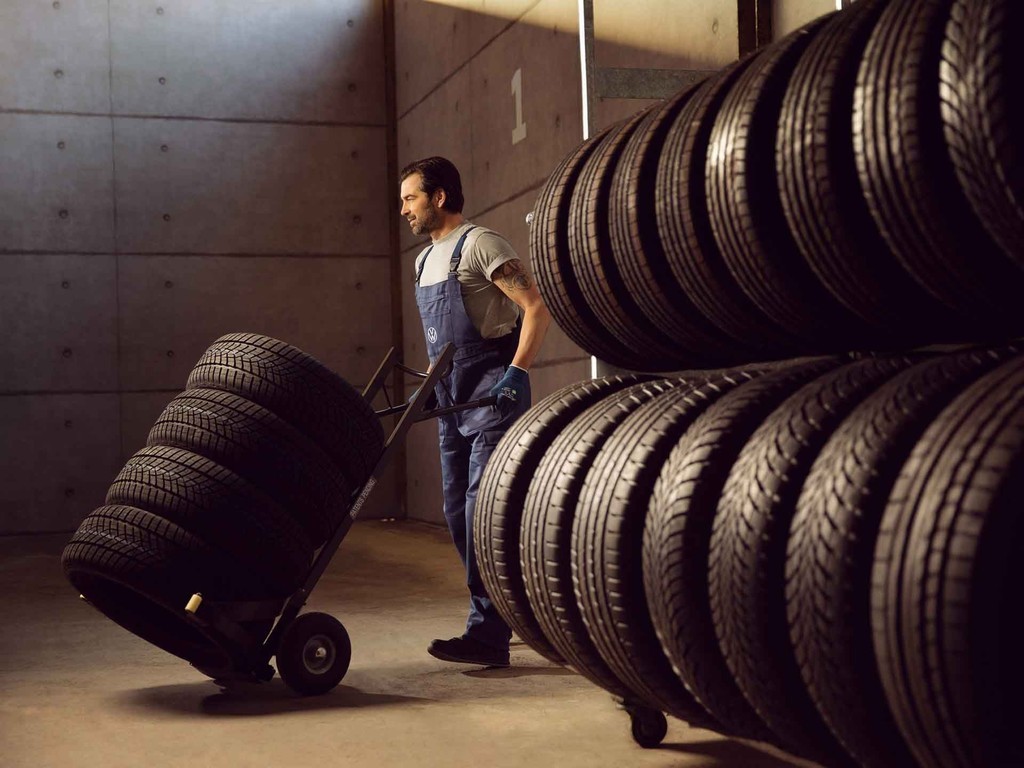 Un operaio di Volkswagen Service trasporta una pila di pneumatici su un carrellino.